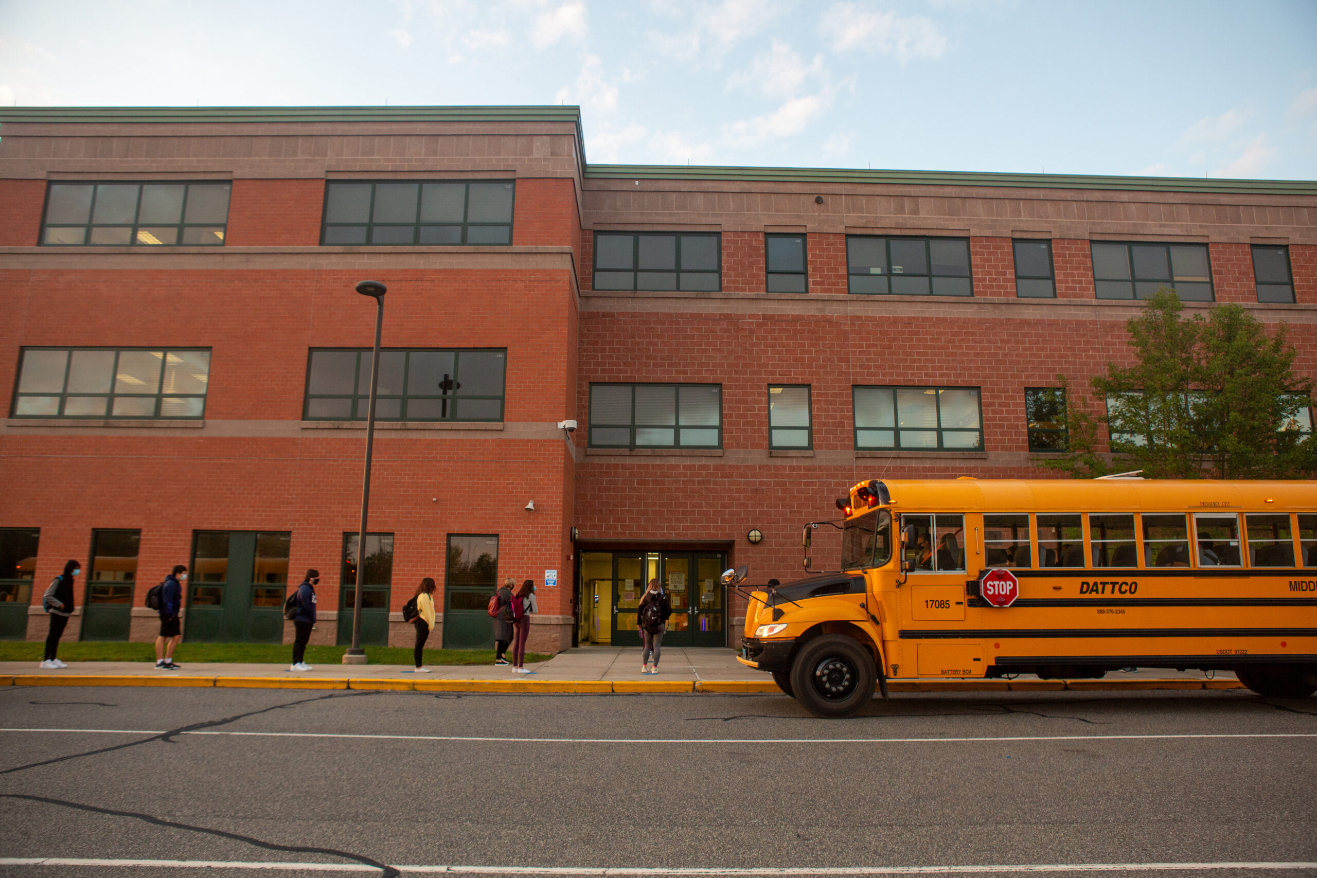 Students line up on socially distanced dots painted on the sidewalk to wait their turn to have their temperatures checked before entering Middletown High School.