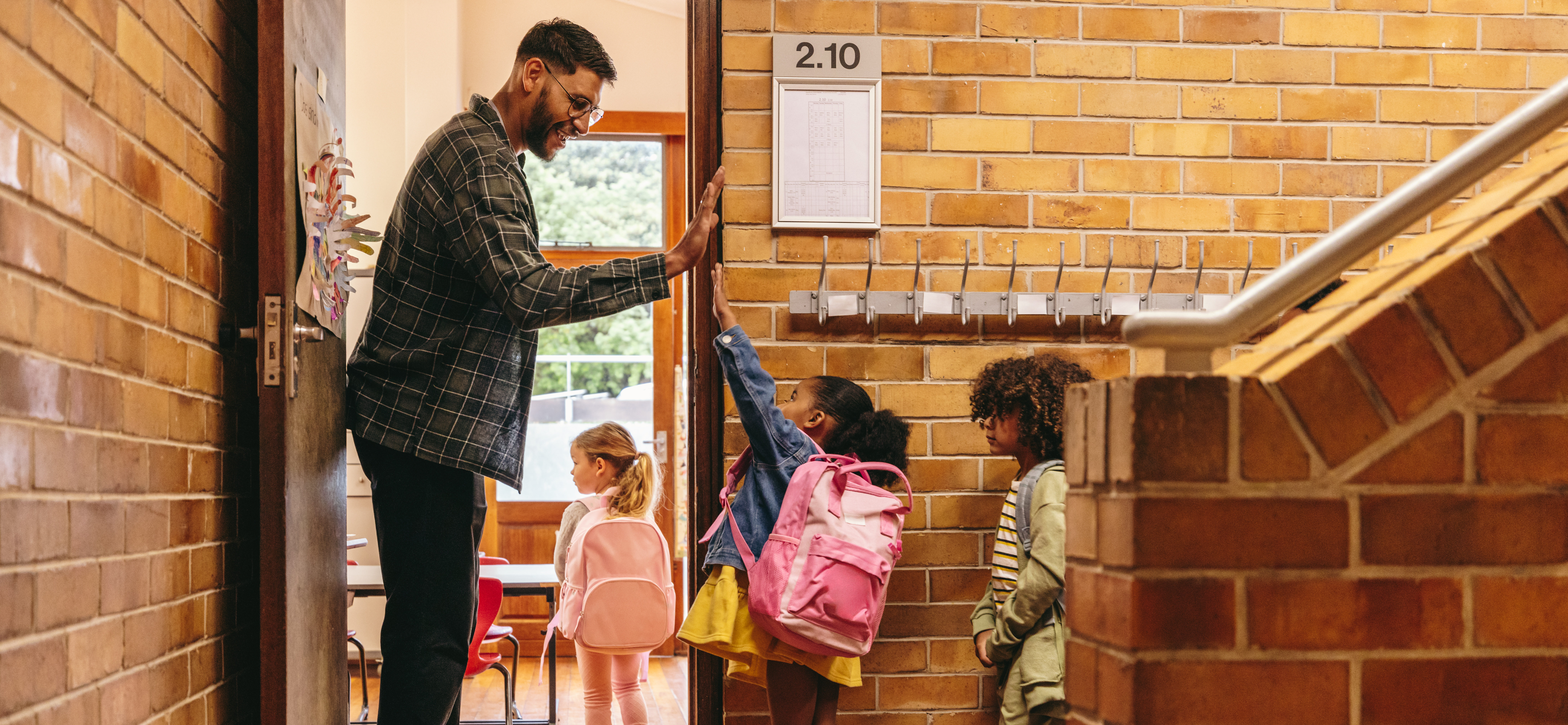 Elementary school teacher greeting his students at the door. Male teacher welcoming his class with a high five