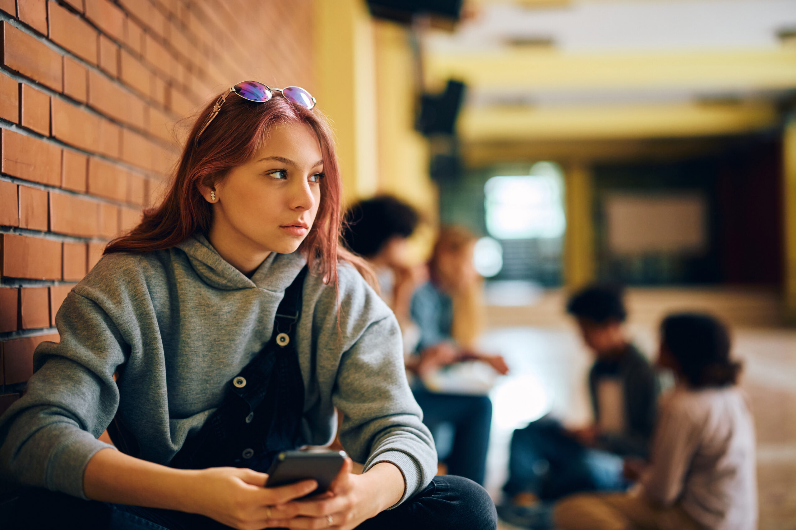 Image of pensive teenage girl using cell phone at high school.
